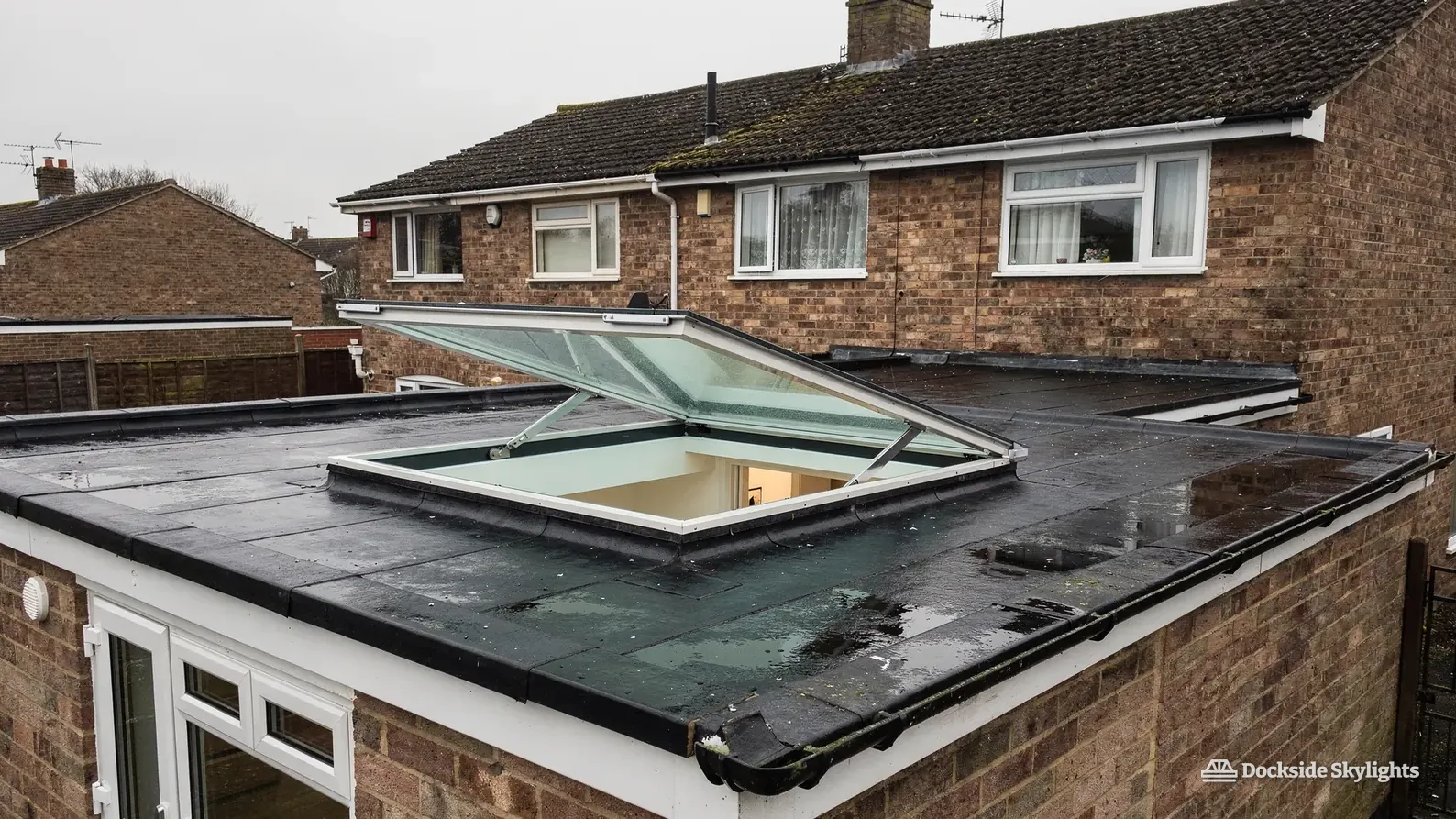 Electric rooflight raised open on a flat roof behind a brick semi