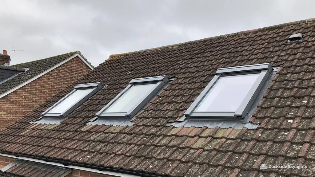 Three roof windows in a row in the brown tiled rear roof of a red-brick house
